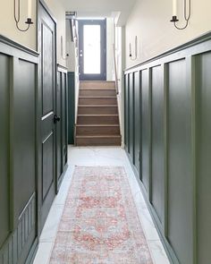 a hallway with green doors and stairs leading up to the second floor, along with a rug on the floor