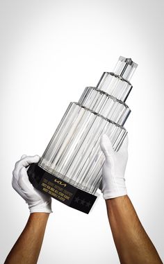 a person holding up a trophy in front of a gray background with white gloves on his hands