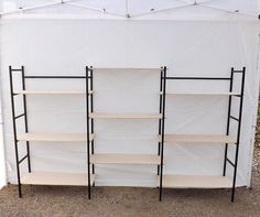 three shelving units in front of a white tent with black legs and shelves on each side