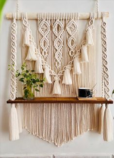 a macrame wall hanging with tassels and potted plant on it