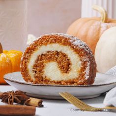 a cinnamon roll sitting on top of a white plate next to pumpkins and spices