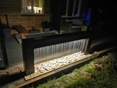 an outdoor fountain in front of a house at night with lights on and grass growing around it