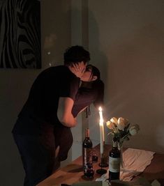 a man and woman kissing in front of a table with pizza, wine bottles and candles