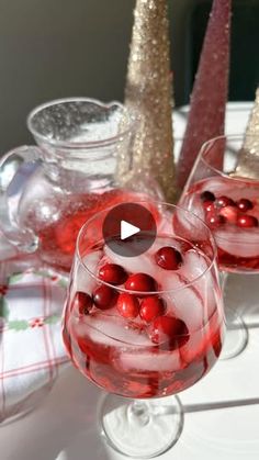 two glasses filled with red liquid and cranberries on top of a white table