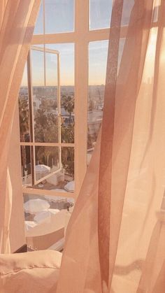 an open window with sheer curtains in front of a cityscape outside the window