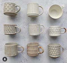 nine white cups and saucers lined up on a gray surface with one cup in the middle