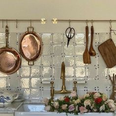 pots and pans hanging on the wall above a kitchen sink with flowers in front of it