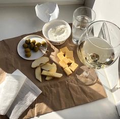 an assortment of cheese and olives on a table next to wine glasses with napkins