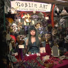 a woman standing in front of a booth with masks on it's display table