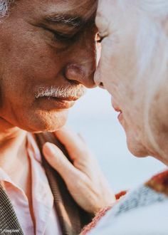 an older man and woman are touching each other's forehead as they stand close together