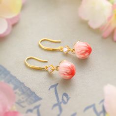 Experience the magic of nature with our Peach Earrings. Featuring a delicate enameled peach adorned with sparkling cubic zirconia, these lovely earrings add a touch of glamour to any style. You'll enjoy the sweetness and cheer of summer they bring to you. Embrace your love for fruit jewelry with these stunning earrings! DETAILS Plating: 18K Gold Materials: 18K Gold on Brass, Enamel, Cubic Zirconia Size: 1.34 "*0.39"(3.4c m*1cm) Weight: 8.3g Peach Flower Shaped Jewelry For Gift, Peach Drop Earrings For Gift, Elegant Adjustable Peach Jewelry, Handmade Peach Dangle Earrings, Peach Round Gemstone Jewelry, Everyday Wear Jewelry, Astrology Jewelry, Peach Earrings, Astrology Necklace