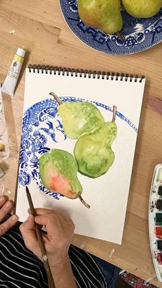 a person is painting some pears on a paper with watercolors and paintbrushes