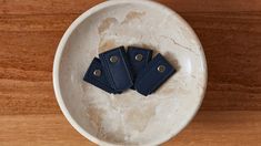 three pieces of blue leather sitting in a white bowl on a wooden surface with metal rivets