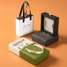 two boxes with necklaces in them sitting on an orange surface next to a white bag