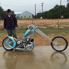 a man standing next to a blue and silver motorcycle on top of a cement ground