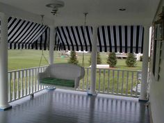 a porch covered in black and white striped awnings next to a green field