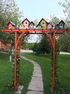 a wooden arch with bird houses on it in the middle of a grassy area next to a path