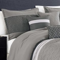 a bed with grey and white comforters on it