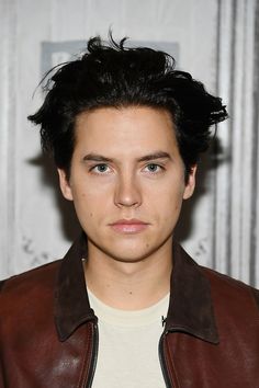 a young man with black hair wearing a brown leather jacket and white t - shirt