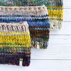 three different colored knitted items sitting on top of a white wooden table next to each other