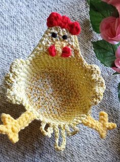 a crocheted chicken sitting on top of a table next to pink flowers