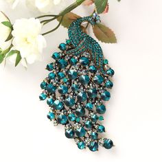 "Gorgeous large rhinestone peacock brooch, which can be used for your DIY project - peacock wedding bridal brooch bouquet, dress accessory, cake decorations, event decor, crafts, scrap booking, jewelry gift and much more! Perfect for peacock theme wedding! Size: 4 1/4\"H x 2 1/4\"W Stones: Teal blue and iridescent Metal color: gold plated This crystal broach can be ordered with pin in the back to add to wedding gown or dress sash, to wire into brooch bouquet, or any number of other craft project Elegant Peacock-colored Brooches For Wedding, Elegant Peacock Brooches For Wedding, Elegant Peacock Color Wedding Brooches, Elegant Wedding Brooch With Peacock Design, Elegant Peacock Design Brooch For Wedding, Elegant Peacock Design Wedding Brooch, Elegant Party Brooch With Peacock Design, Peacock Colored Wedding Brooch Jewelry, Wedding Brooch With Peacock Design