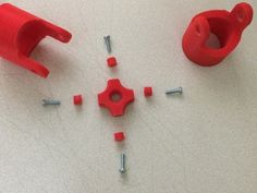 some red plastic parts and screws are laying on the table together with one pointing at the other