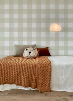 a bed with a teddy bear pillow on it's head in front of a checkered wall