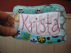 a person holding up a small patch with the word krista written on it in red