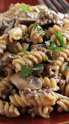 a red plate topped with pasta covered in meat and mushrooms, garnished with parsley