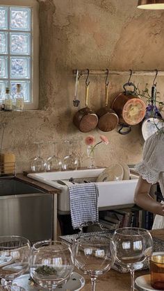 a woman standing in front of a kitchen counter filled with dishes and wine glasses on it