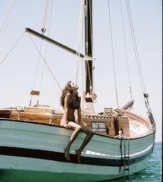 a woman sitting on the bow of a sailboat in the ocean with her legs hanging out