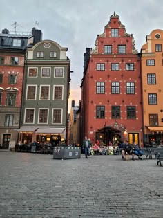 people sitting on benches in the middle of a cobblestone street lined with buildings