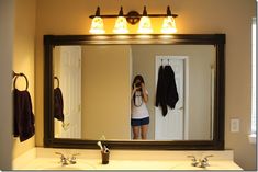 a woman taking a selfie in front of a bathroom mirror with lights on above it