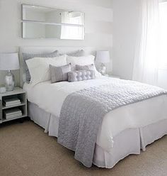 a bedroom with white and gray bedding, mirror on the wall and nightstands