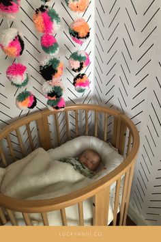 a baby sleeping in a crib next to a wall with pom poms