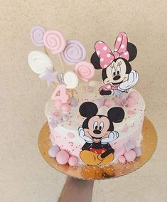 a person holding a cake with mickey and minnie mouse decorations on it, in front of a wall