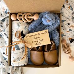 a blue teddy bear sitting in a box next to some baby shoes and a sign that says welcome to the world