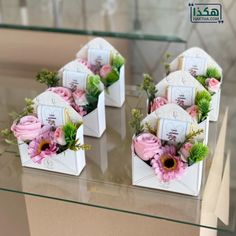 four small white boxes with flowers in them on a glass table, one is empty and the other has pink roses