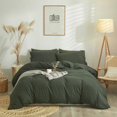 a bed with green comforter and pillows in a white room next to a chair