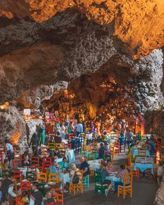 many people are sitting at colorful tables and chairs in a cave like area with large rocks