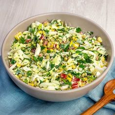 a bowl filled with salad next to a wooden spoon on top of a blue towel