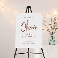 a welcome sign sitting on top of a easel next to a vase with flowers