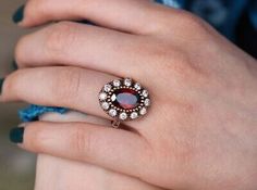 a woman's hand wearing a ring with an oval shaped stone surrounded by small diamonds