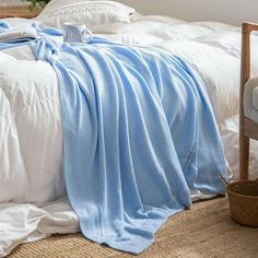 an unmade bed with white sheets and blue blankets on it, next to a chair