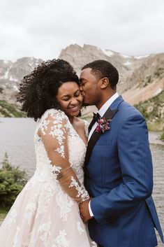 a bride and groom standing next to each other in front of a body of water