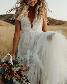 a woman in a white dress is holding a flower bouquet and posing for the camera