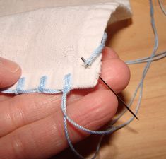 a hand holding a piece of cloth with a needle in it and some thread on the end