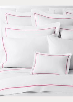 a bed with white sheets and pink trimmings on the pillowcase, along with two pillows