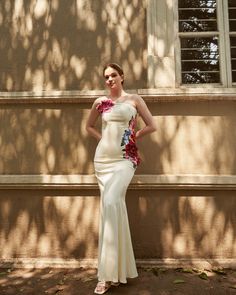 a woman standing in front of a building wearing a white dress with flowers on it